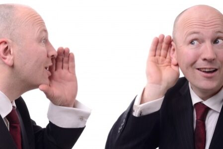 Man with his hand cupping his ear as another identical man cups his mouth saying something to him