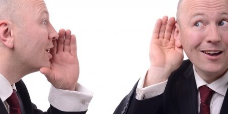 Man with his hand cupping his ear as another identical man cups his mouth saying something to him