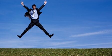 Man in a business suit jumping in the air with his hands up out in a field
