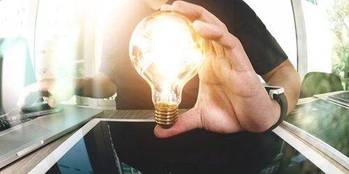 Man holding up a lightbulb that is lit on top of a tablet