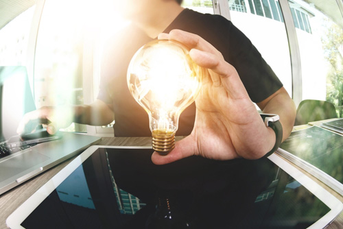 Man holding up a lightbulb that is lit on top of a tablet