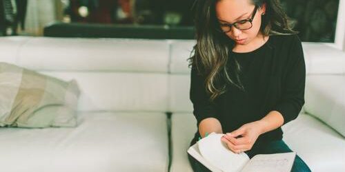 woman on couch wearing glasses with notebook