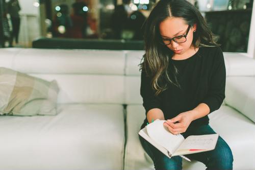 woman on couch wearing glasses with notebook