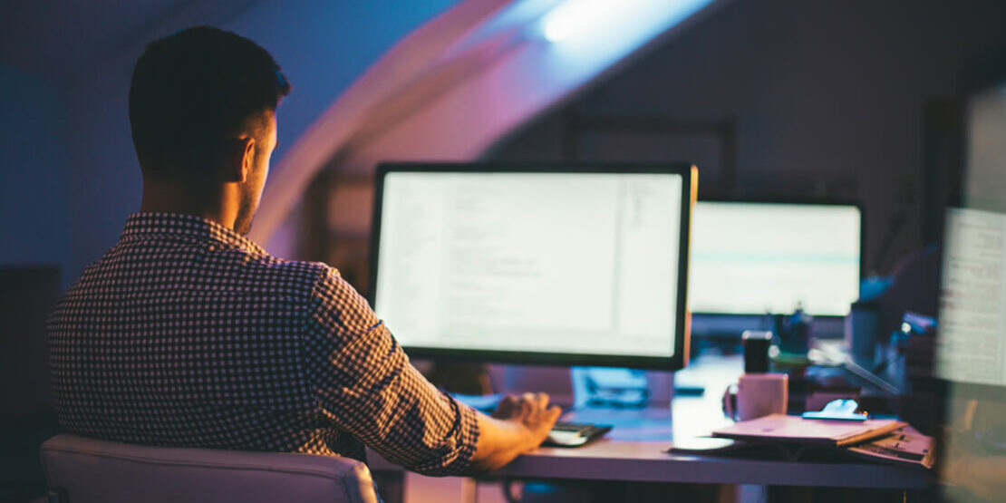 man working alone at his computer in a dark office