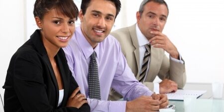 Three people in business attire sitting at a table smiling towards the camera