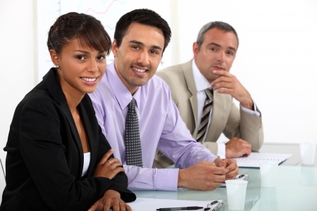Three people in business attire sitting at a table smiling towards the camera