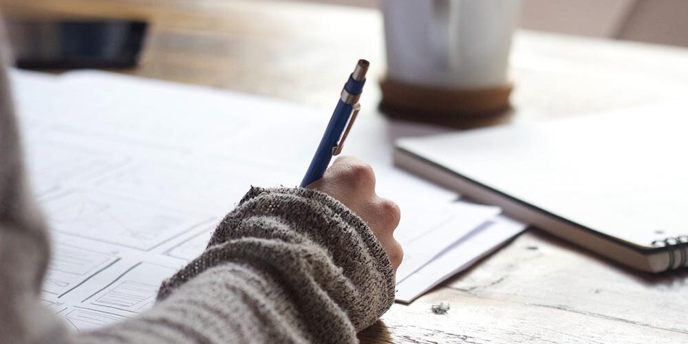 coffee on desk with person writing on papers