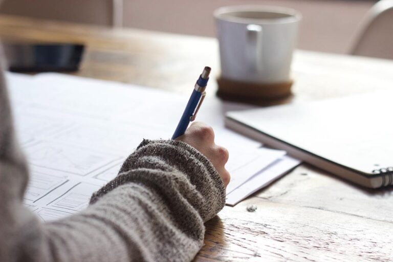 coffee on desk with person writing on papers