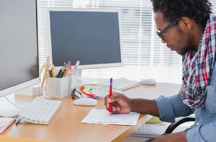 man drawing on a piece of paper at his desk