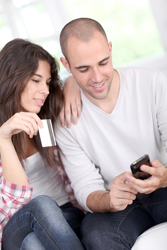 Man looking at his phone as a girl sits next to him holding a credit card