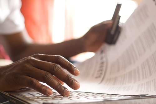 woman looking at papers as she works on her laptop