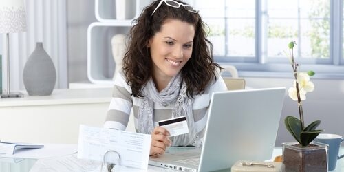 woman smiling at her laptop holding a card