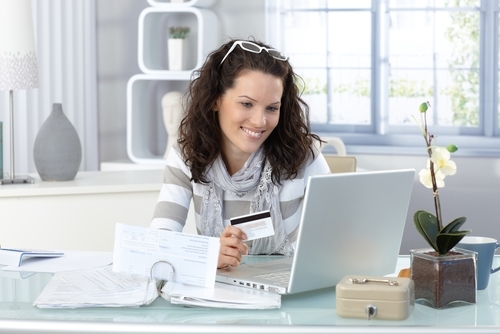 woman smiling at her laptop holding a card