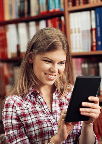 Woman smiling in a library scrolling on a tablet