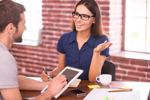 woman talking to a man as he listens and looks at his tablet