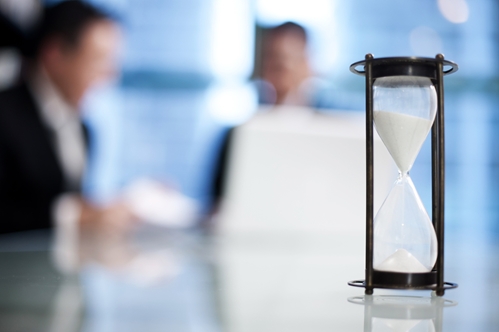 two people looking at paperwork with a sand timer in the foreground