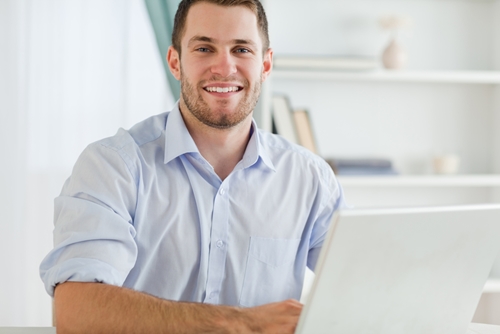 man smiling at the camera as he works on a laptop