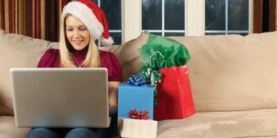 woman in a santa hat working on her laptop with gifts beside her