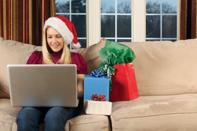 woman in a santa hat working on her laptop with gifts beside her