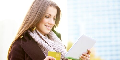 Woman holding a tablet in one hand and a credit card in the other outside