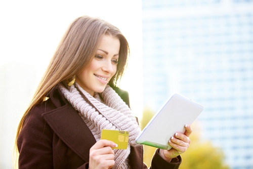 Woman holding a tablet in one hand and a credit card in the other outside