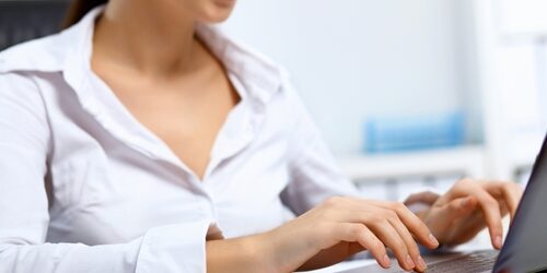 Woman in a white button up working on a laptop