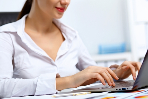 Woman in a white button up working on a laptop