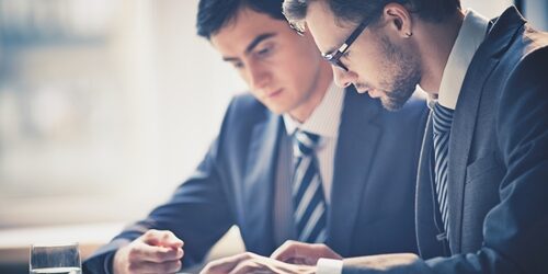 two men looking at a tablet at a table