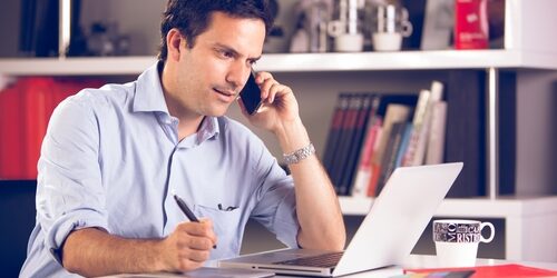 a man on his phones as he works on his laptop at his desk