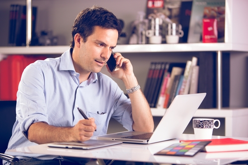 a man on his phones as he works on his laptop at his desk