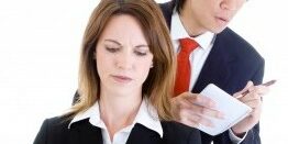 woman working on her computer with a man looking over her shoulder writing something down on a notepad