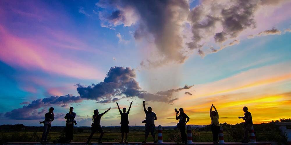 Group of 8 people posing in front of a colorful sunset