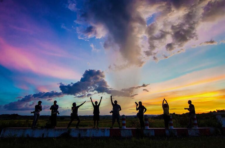 Group of 8 people posing in front of a colorful sunset
