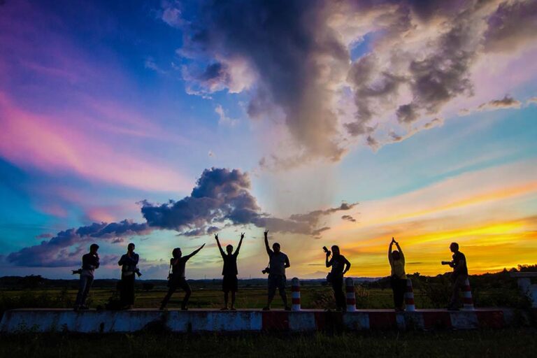 Group of 8 people posing in front of a colorful sunset