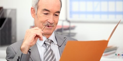 Man with his glasses in his mouth as he look in folder