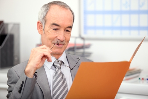 Man with his glasses in his mouth as he look in folder