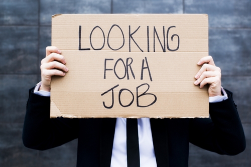 Man holding up a cardboard sign saying he is looking for a job in front of his face as he is dressed in a suit