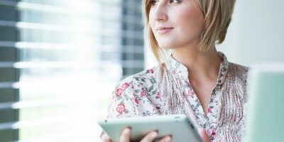 woman looking out the window as she works on a tablet