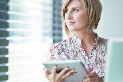 woman looking out the window as she works on a tablet