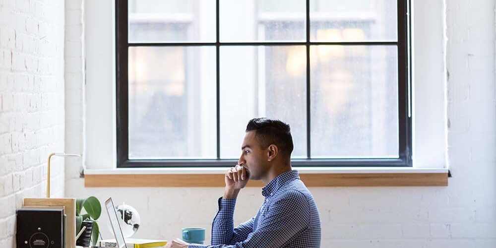 man working at his desk on a laptop in front of a window