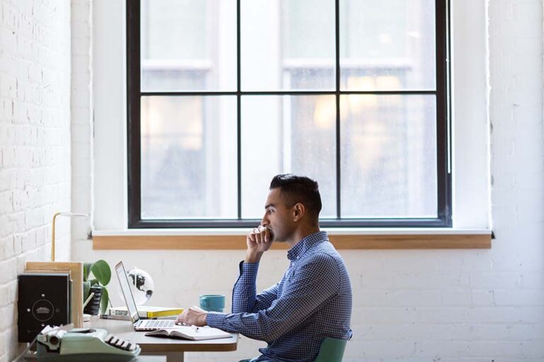 man working at his desk on a laptop in front of a window