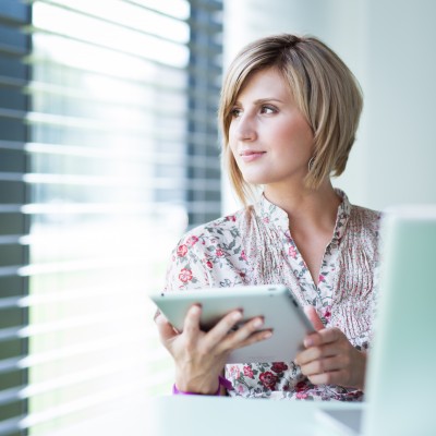 woman looking out the window as she works on a tablet