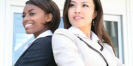 two women back to back with their arms crossed posing