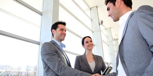 two men shaking hands with woman smiling next to one of them