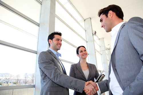 two men shaking hands with woman smiling next to one of them