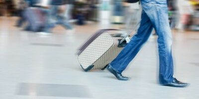 Man walking through an airport with luggage behind him, pictured is blurred