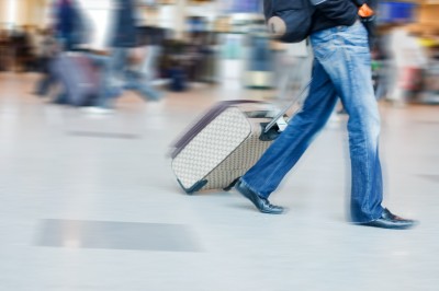 Man walking through an airport with luggage behind him, pictured is blurred