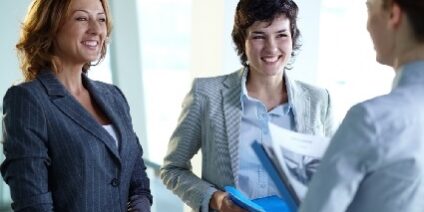 two women smiling at another as they talk in an office setting