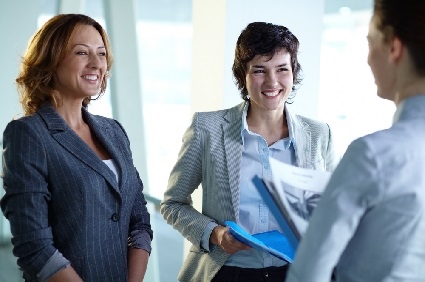 two women smiling at another as they talk in an office setting