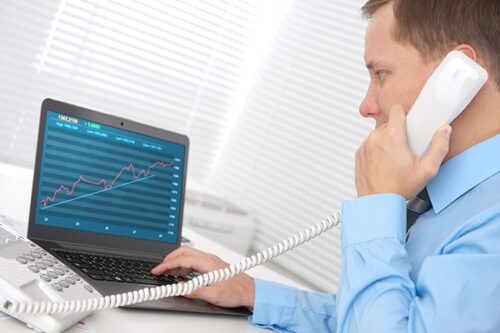 Man on a phone looking at a graph of his computer